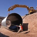 a crane moving a pipe with the help of a worker in a construction site