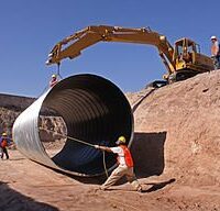 a crane moving a pipe with the help of a worker in a construction site