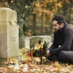 Mid adult man with flowers and candles visiting graves at the cemetery.